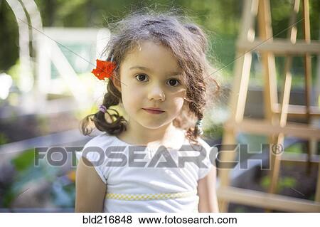 Stock Photo - Smiling girl wearing flower in hair in garden. Fotosearch