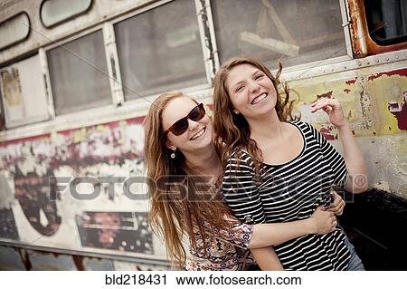 Stock Image - Smiling girls hugging near dilapidated bus. Fotosearch