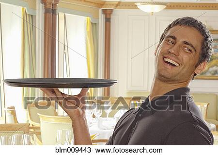 Stock Image - Smiling Hispanic waiter carrying tray. Fotosearch