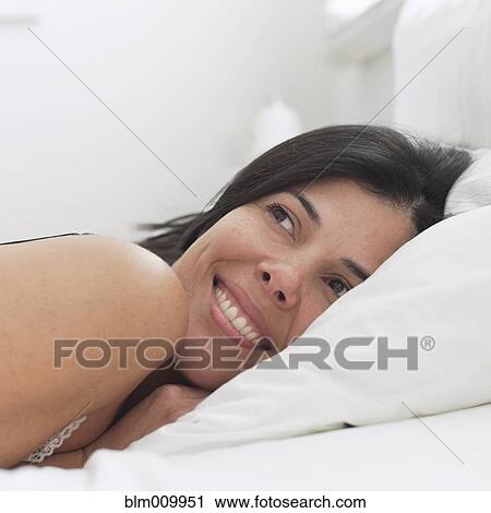Stock Image - Smiling Hispanic woman laying in bed. Fotosearch