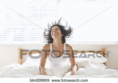 Stock Photo - Smiling Hispanic woman sitting in bed. Fotosearch