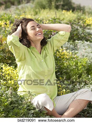 Stock Image - Smiling Hispanic woman sitting in garden. Fotosearch