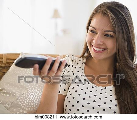Stock Image - Smiling Indian woman using remote control. Fotosearch
