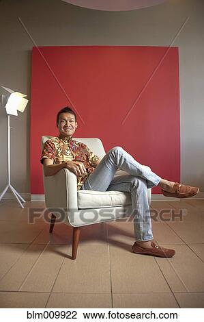 Stock Image - Smiling Malaysian man sitting in armchair. Fotosearch