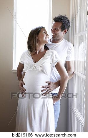 Stock Photograph - Smiling man holding belly of pregnant wife. Fotosearch