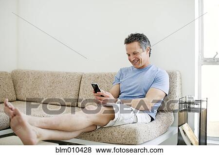 Stock Photo - Smiling man text messaging on cell phone in living room. Fotosearch