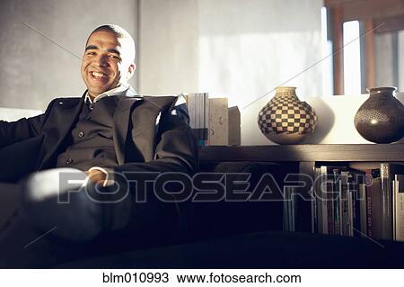 Stock Image - Smiling mixed race businessman sitting in chair. Fotosearch