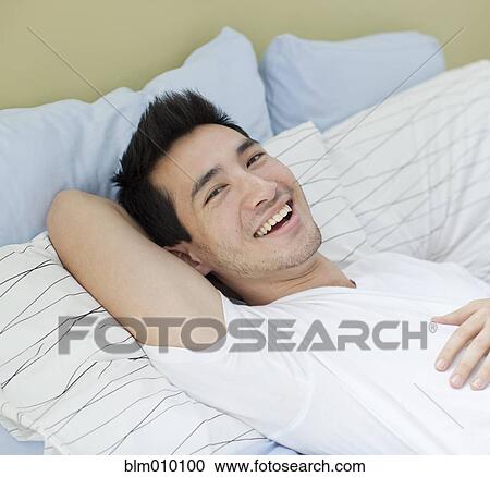 Stock Image - Smiling mixed race man laying in bed. Fotosearch