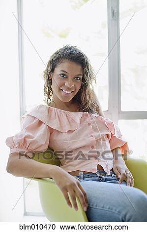 Stock Image - Smiling mixed race woman sitting in chair. Fotosearch