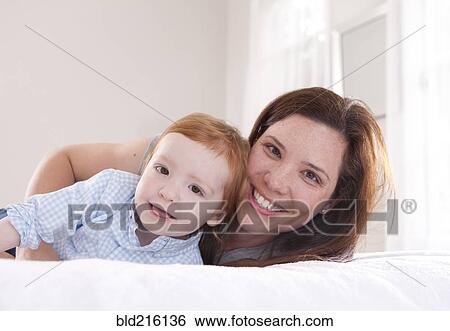 Stock Photograph - Smiling mother and son hugging on bed. Fotosearch