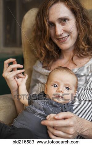 Stock Image - Smiling mother holding baby in armchair. Fotosearch