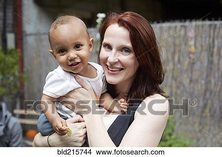 Picture - Smiling mother holding baby son in backyard. Fotosearch
