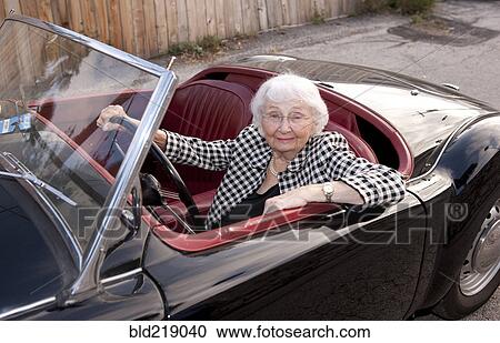 Stock Image - Smiling older woman driving convertible. Fotosearch