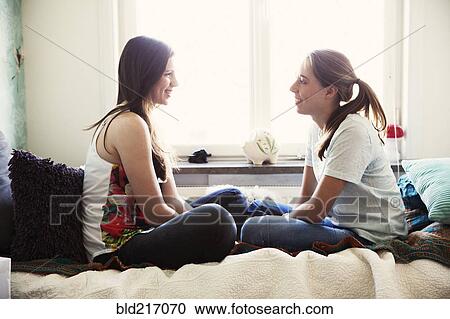 Stock Image - Smiling sisters talking on bed. Fotosearch