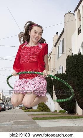 Stock Image - Smiling teenage girl jumping with plastic hoop. Fotosearch