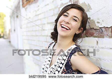 Stock Photography - Smiling teenage girl leaning on brick wall. Fotosearch