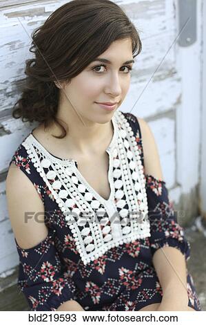 Stock Image - Smiling teenage girl leaning on wooden wall. Fotosearch