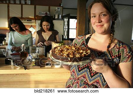 Stock Image - Smiling woman holding cake in kitchen. Fotosearch