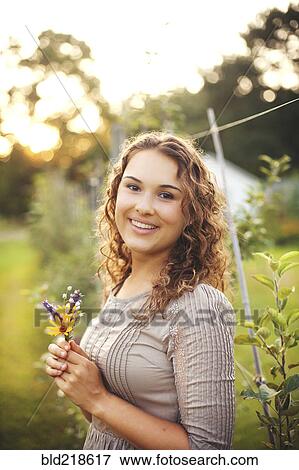 Smiling woman holding flower in garden View Large Photo Image Stock Photo - Smiling woman holding flower in garden. Fotosearch