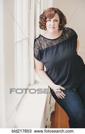Stock Image - Smiling woman leaning on windowsill. Fotosearch