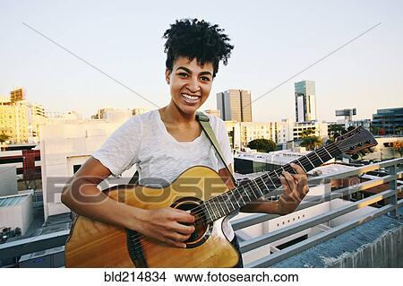 Smiling woman playing guitar on urban rooftop View Large Photo Image Picture - Smiling woman playing guitar on urban rooftop. Fotosearch