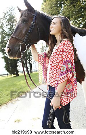 Stock Photo - Smiling woman walking horse on dirt path. Fotosearch