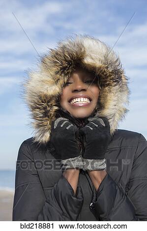 Stock Image - Smiling woman wearing coat on beach. Fotosearch