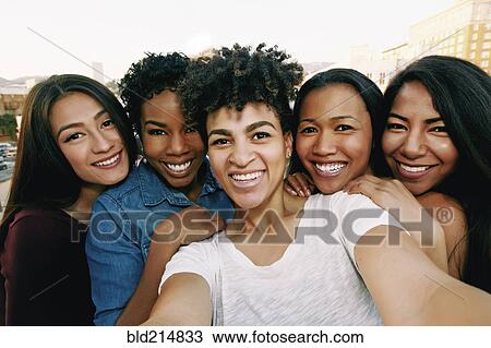 Stock Image - Smiling women taking selfie on urban rooftop. Fotosearch