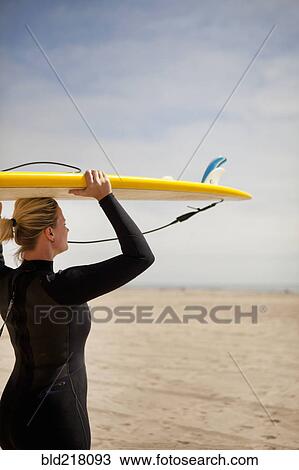 Stock Image - Surfer carrying surfboard on beach. Fotosearch