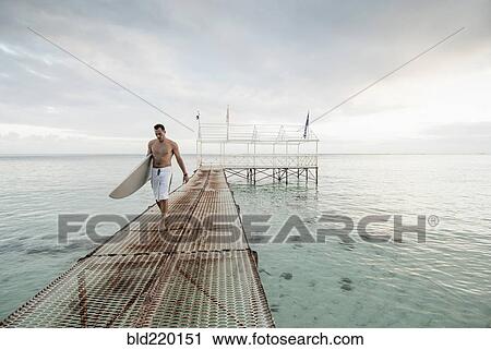 Surfer carrying surfboard on metal dock over ocean View Large Photo Image Stock Image - Surfer carrying surfboard on metal dock over ocean. Fotosearch
