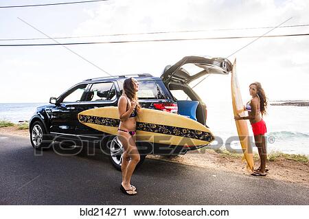 Stock Image - Surfers unloading surfboards from car near beach. Fotosearch