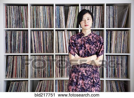 Stock Image - Taiwanese woman standing near record collection. Fotosearch