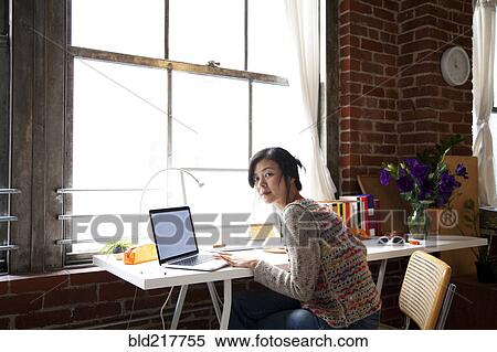 Stock Photography - Taiwanese woman using laptop in home office. Fotosearch