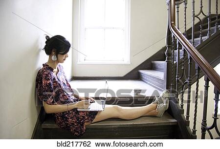 Stock Image - Taiwanese woman using laptop on staircase. Fotosearch