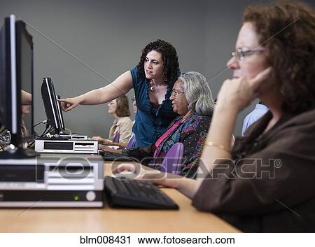 Stock Image - Teacher helping students on computers in computer lab. Fotosearch