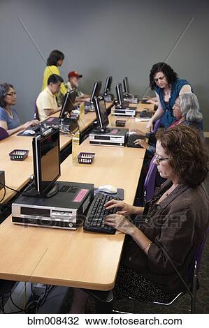 Stock Image - Teacher helping students on computers in computer lab. Fotosearch