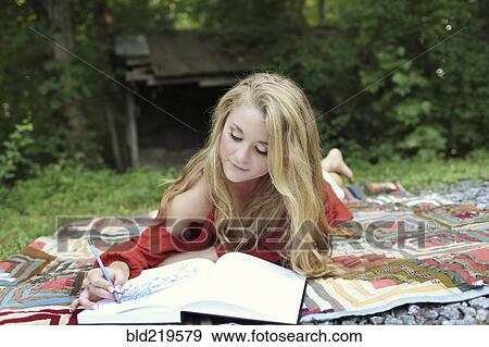 Stock Photo - Teenage girl drawing in notebook on blanket. Fotosearch