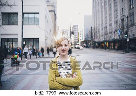 Stock Photo - Teenage girl standing with arms crossed in city intersection. Fotosearch