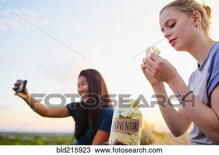 Stock Image - Teenage girls photographing and relaxing outdoors. Fotosearch