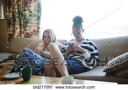 Stock Photo - Teenage girls using cell phones on sofa. Fotosearch