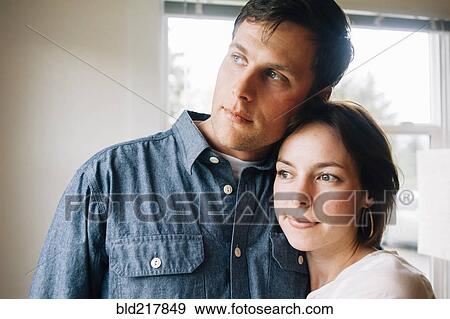 Thoughtful couple hugging near window View Large Photo Image Stock Photo - Thoughtful couple hugging near window. Fotosearch
