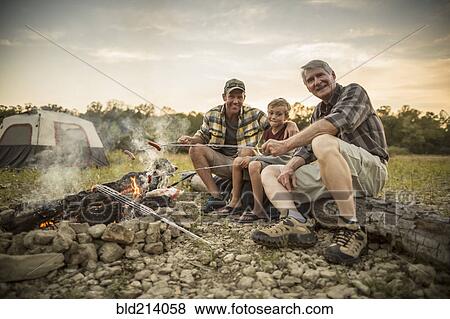 Three generations of Caucasian men roasting hot dogs over campfire View Large Photo Image Stock Photo - Three generations of Caucasian men roasting hot dogs over campfire. Fotosearch