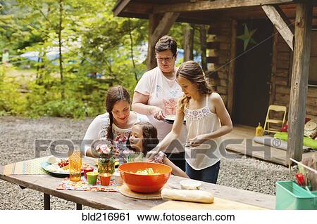 Stock Image - Three generations of Caucasian women cooking outside cabin. Fotosearch
