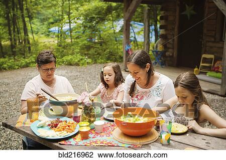 Stock Image - Three generations of Caucasian women eating outside cabin. Fotosearch