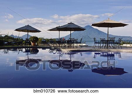 Stock Photograph - Umbrellas, tables and chairs at poolside. Fotosearch