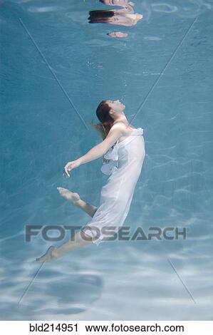 Stock Image - Underwater view of Caucasian woman in dress swimming in pool. Fotosearch