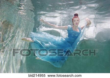 Stock Photography - Underwater view of Caucasian woman in dress swimming in pool. Fotosearch