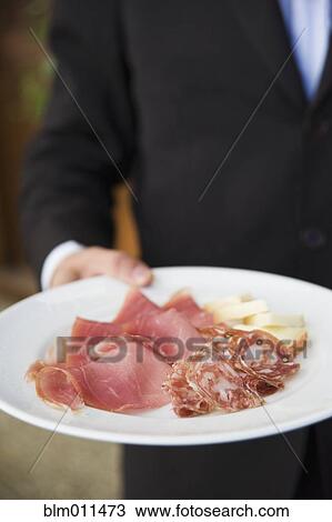 Stock Image - Waiter carrying plate of cured Italian meats. Fotosearch