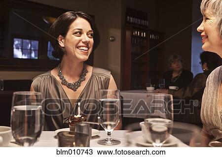 Stock Image - Woman about to blow out birthday cupcake in restaurant. Fotosearch