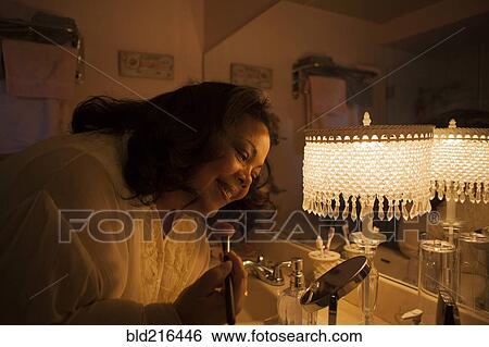 Stock Photograph - Woman applying makeup in bathroom mirror. Fotosearch